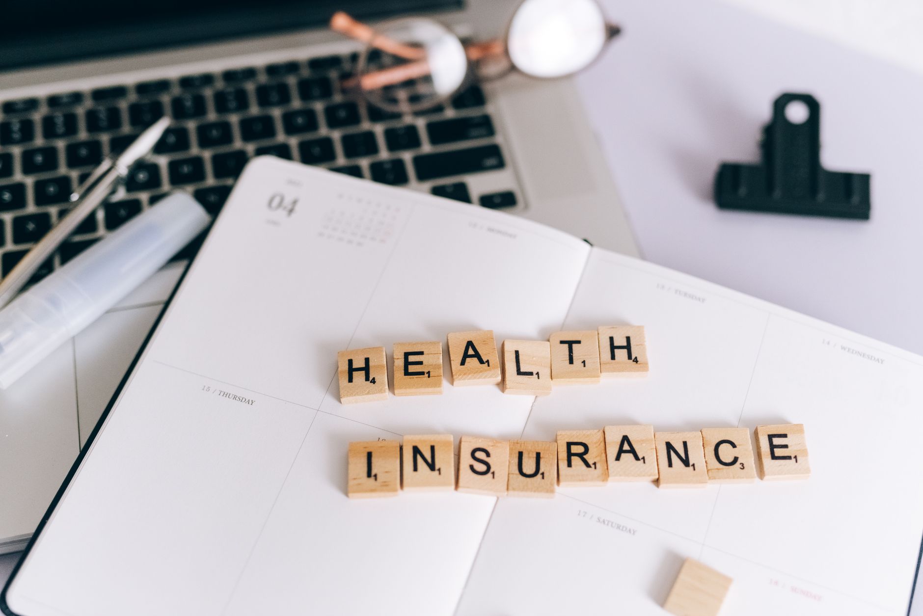 Klocki scrabble z napisem health insurance na planerze obok laptopa