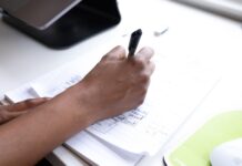 Jak napisać skuteczny biznesplan krok po kroku: praktyczny przewodnik dla początkujących przedsiębiorców Osoba przy biurku robi notatki do biznesplanu na kartkach papieru