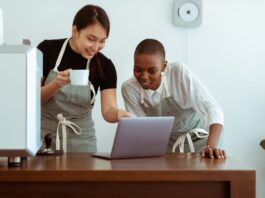 Jak sztuczna inteligencja zmienia codzienną pracę w małych i średnich firmach Kelnerki w kawiarni przeglądają laptop na wspólnym stoliku
